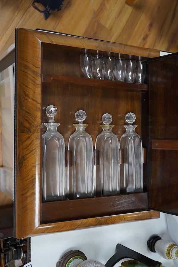 Asprey of London, a cushion-moulded walnut decanter wall cabinet, chromolithograph enclosing four cut glass decanters and six shot glasses, 57cm high, 37.5cm wide. Condition - good.